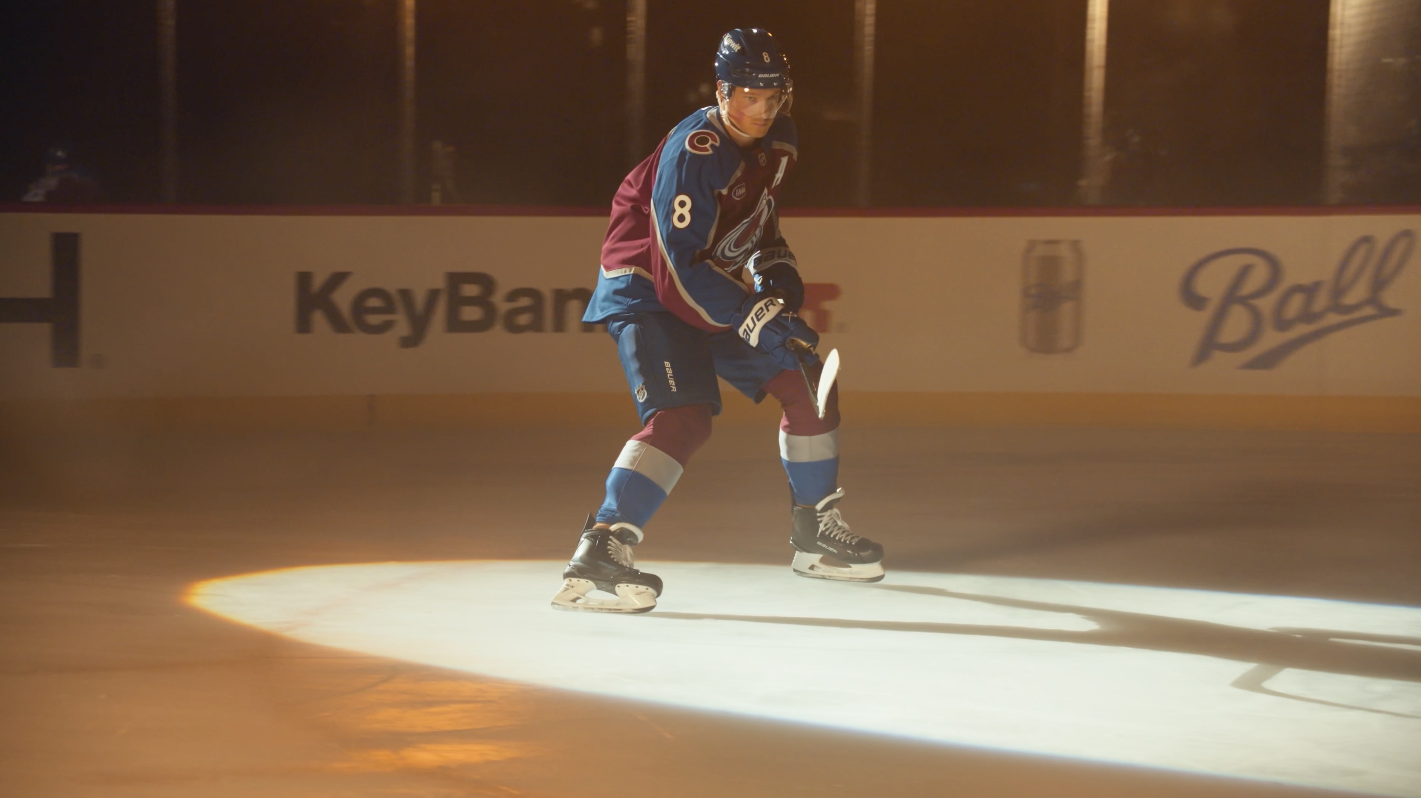Cale Makar speeds past the camera in his Colorado Avalanche uniform, illuminated by a bold spotlight that highlights motion and energy on the ice.