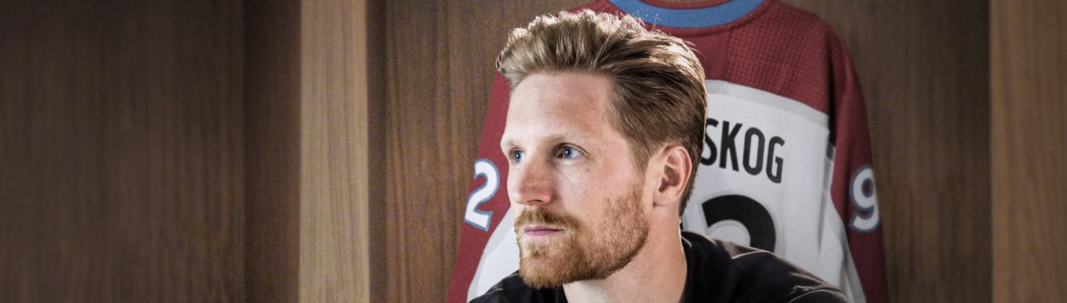 Gabe Landeskog sits in a hockey locker room and looks pensively up to the right. His jersey with the number 92 hangs behind him.