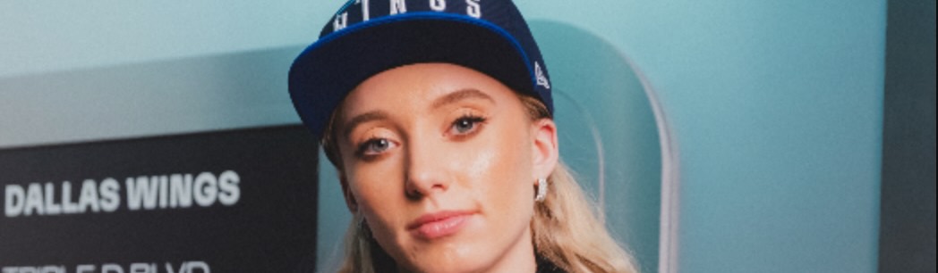 Paige Bueckers poses with the W train behind her wearing a Dallas Wings hat