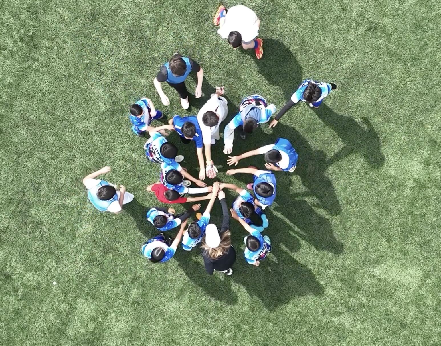 Overhead drone shot on a turf field with middle school soccer players putting their hands in before a big game