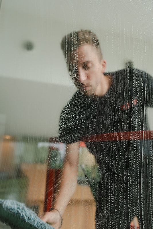 Jonge man die een glas schoonmaakt met een raamwisser in een binnenruimte.