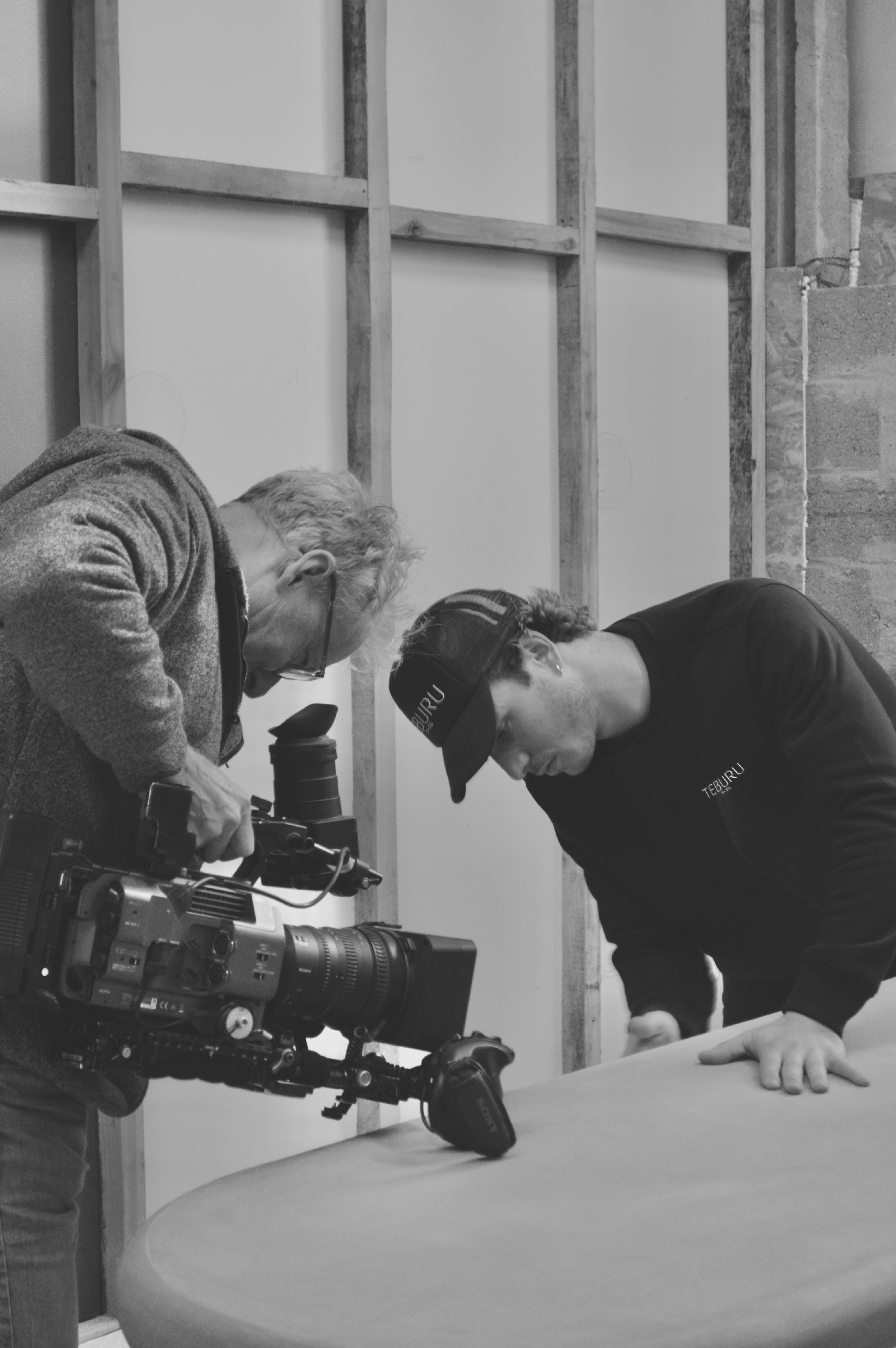 A man showing the table he created to another man holding a camera close to the table