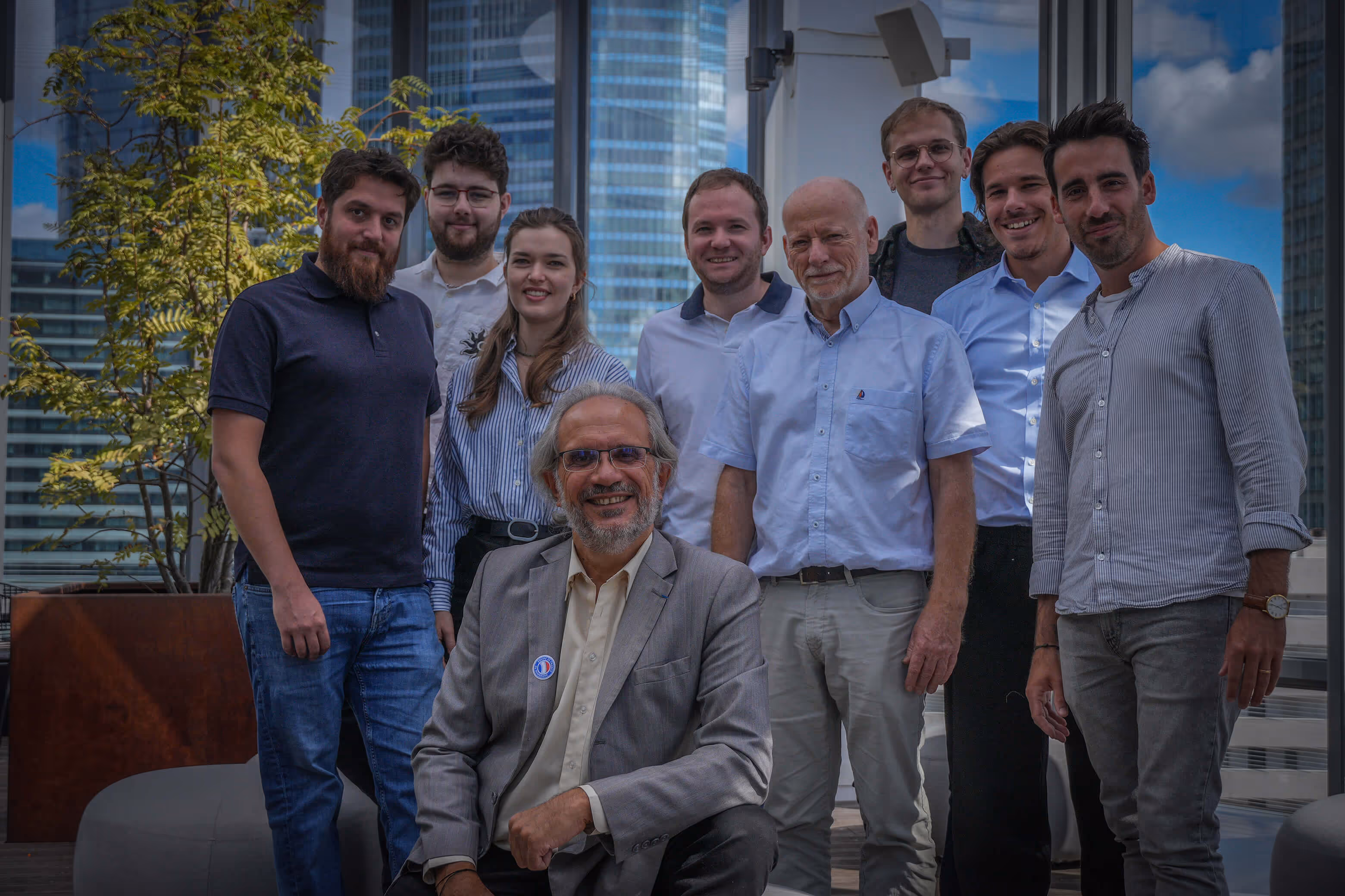 Groupe de neuf personnes posant ensemble sur une terrasse urbaine avec des gratte-ciels en arrière-plan.