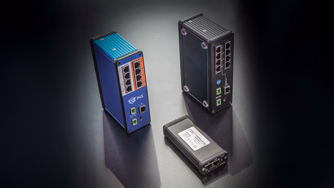 Trois dispositifs électroniques industriels avec plusieurs ports réseau posés sur une surface sombre.