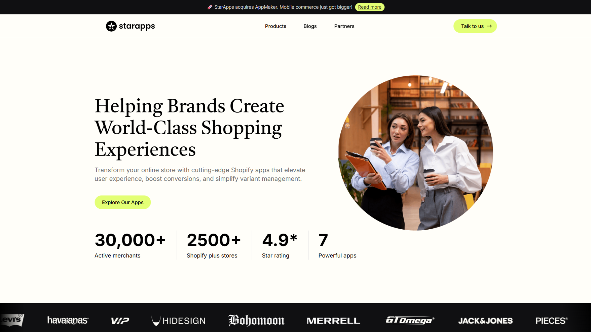 starapps website homepage featuring the starapps logo, top announcement banner stating StarApps acquires AppMaker, navigation links, headline Helping Brands Create World-Class Shopping Experiences, subheading about cutting-edge Shopify apps, an Explore Our Apps button, a circular photo of business professionals, key metrics including 30,000+ active merchants, 2500+ Shopify Plus stores, 4.9-star rating, and 7 powerful apps, alongside brand logos such as Levi's, Havaianas, VIP, Hidesign, Bohomoon, Merrell, Omega, Jack & Jones, and Pieces.