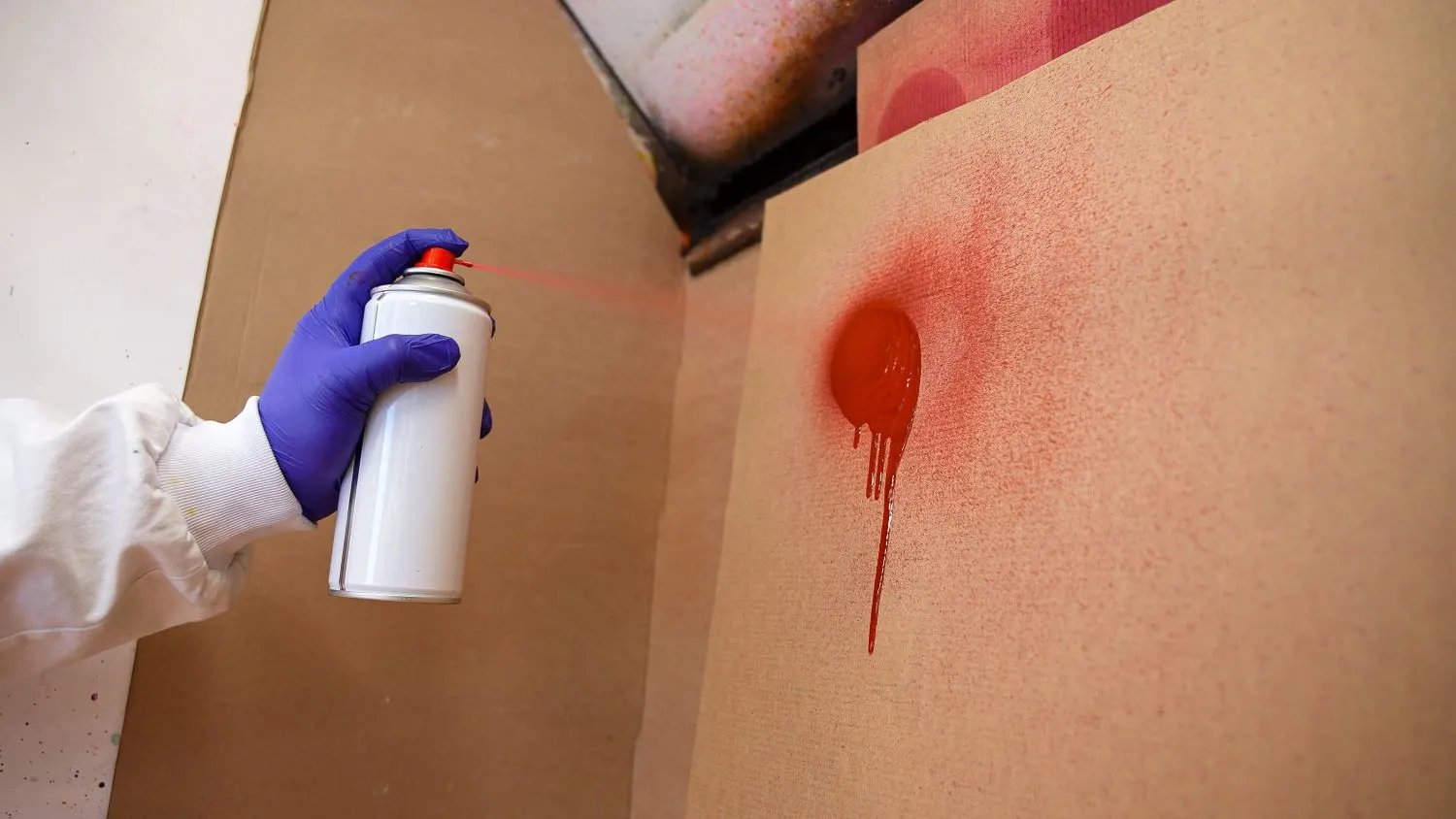 Hånd, der sprayer med rød maling på en væg