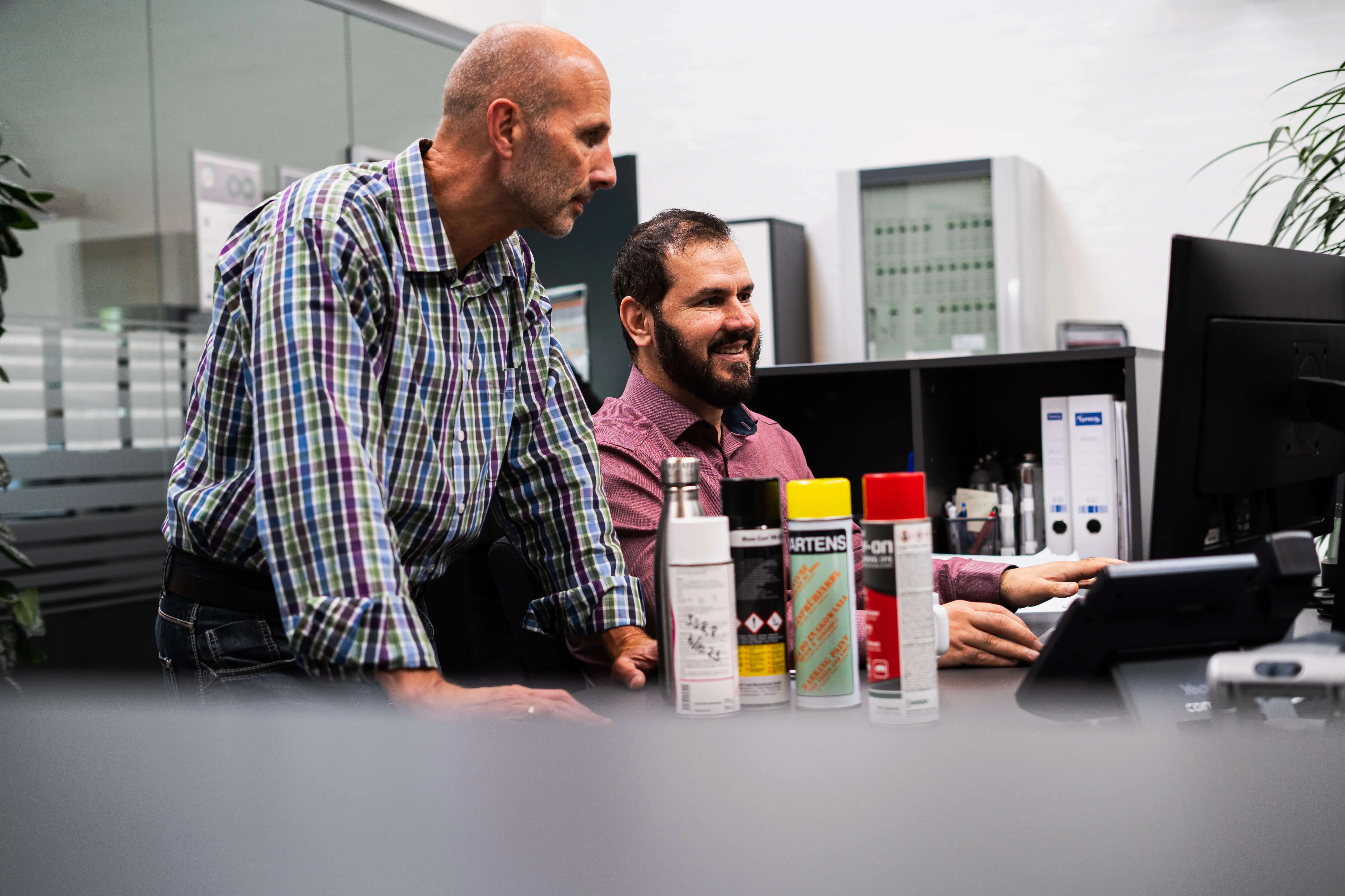 Two men sitting at desk looking into a PC screen