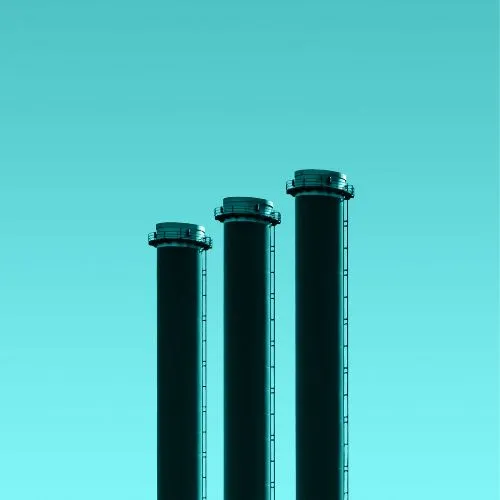 Three tall industrial chimneys standing against a clear blue sky.