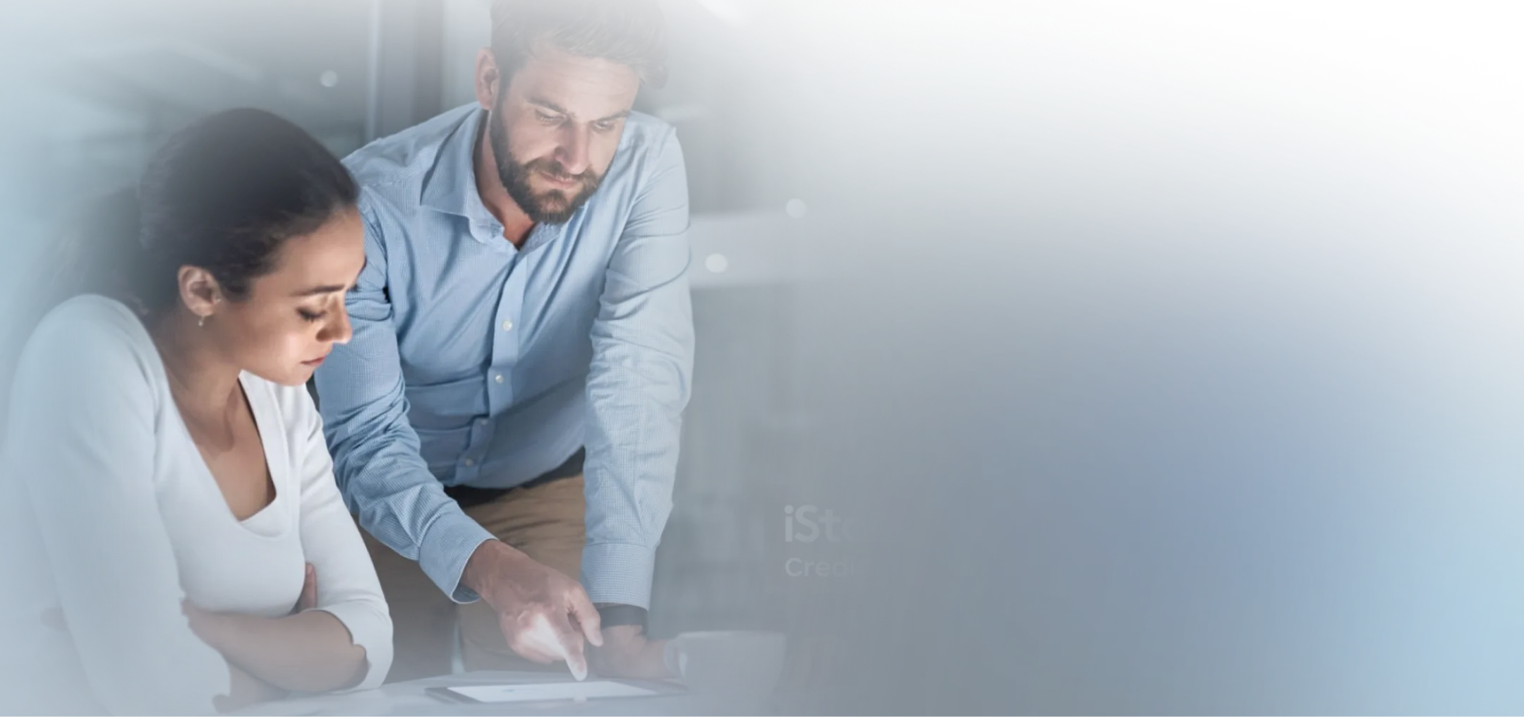 Man in a blue shirt explaining something on a tablet to a woman in a white top at a table.