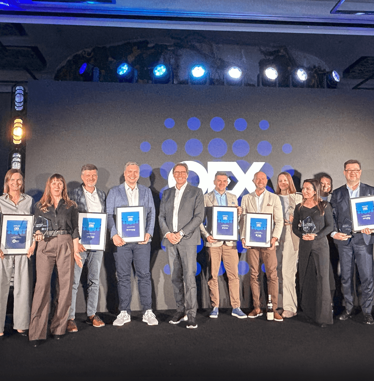 Group photo of OEX employees holding awards on stage during the OEX Day conference.