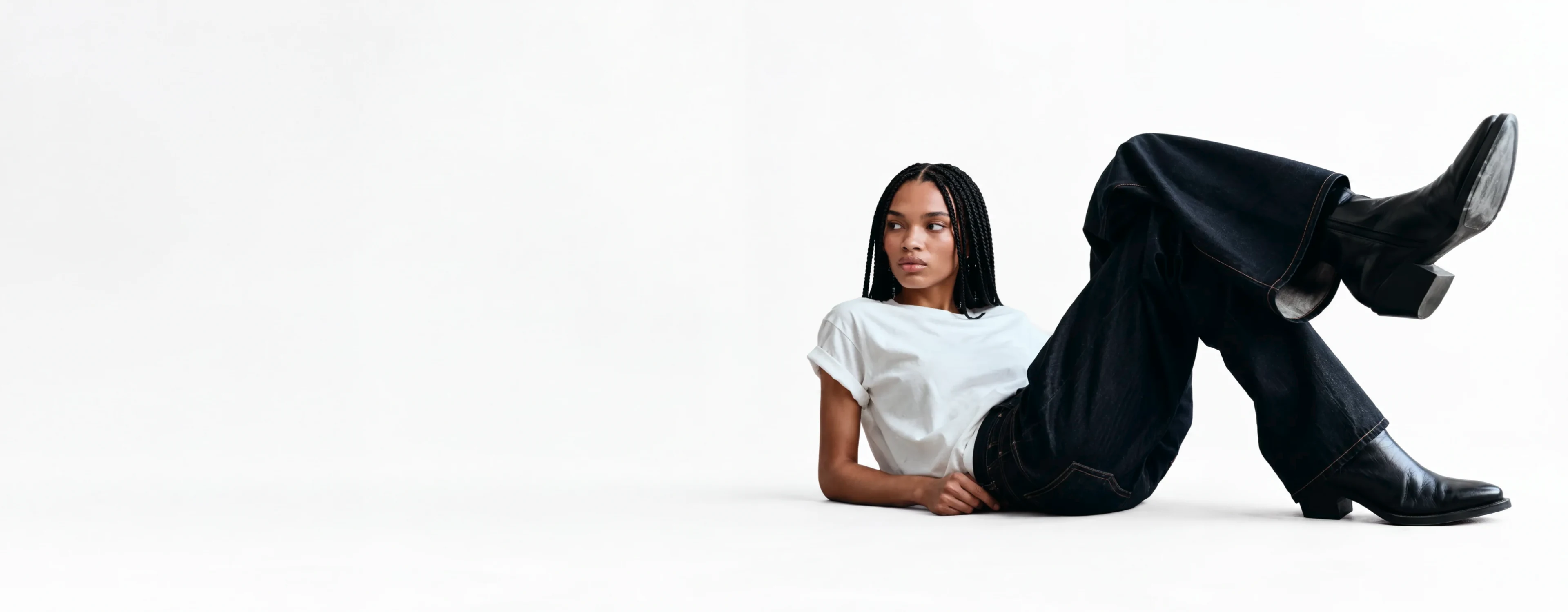 AI generated model in a white tee and dark flared jeans reclining on a pale studio floor