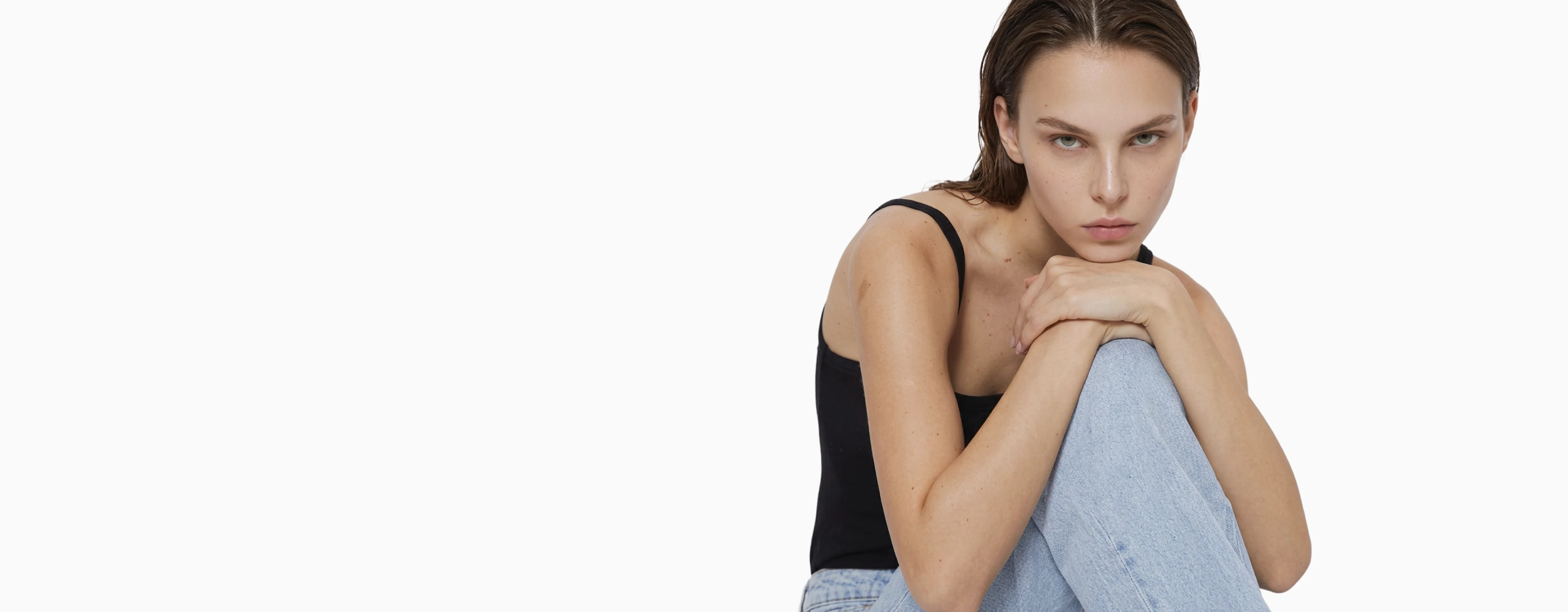 AI generated model in a black tank top and light jeans seated against a pale studio background
