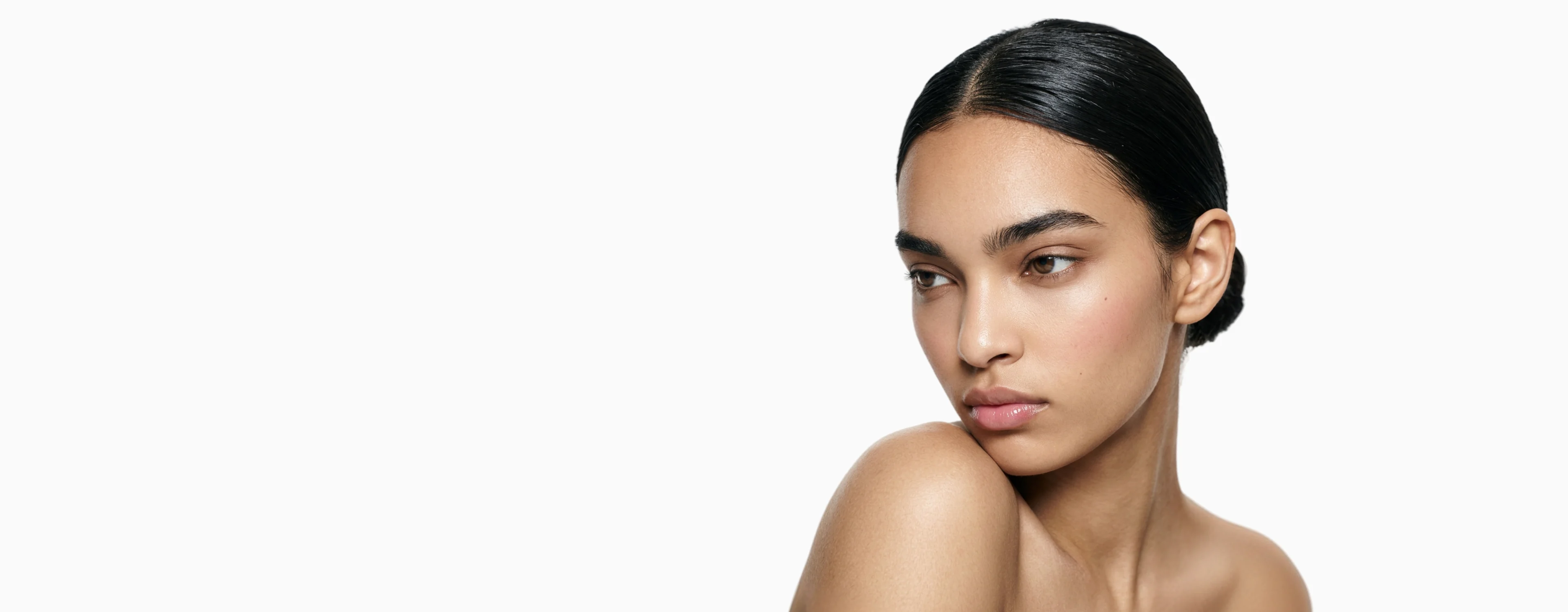 AI generated model with dark hair swept back and a bare shoulder against a pale studio background