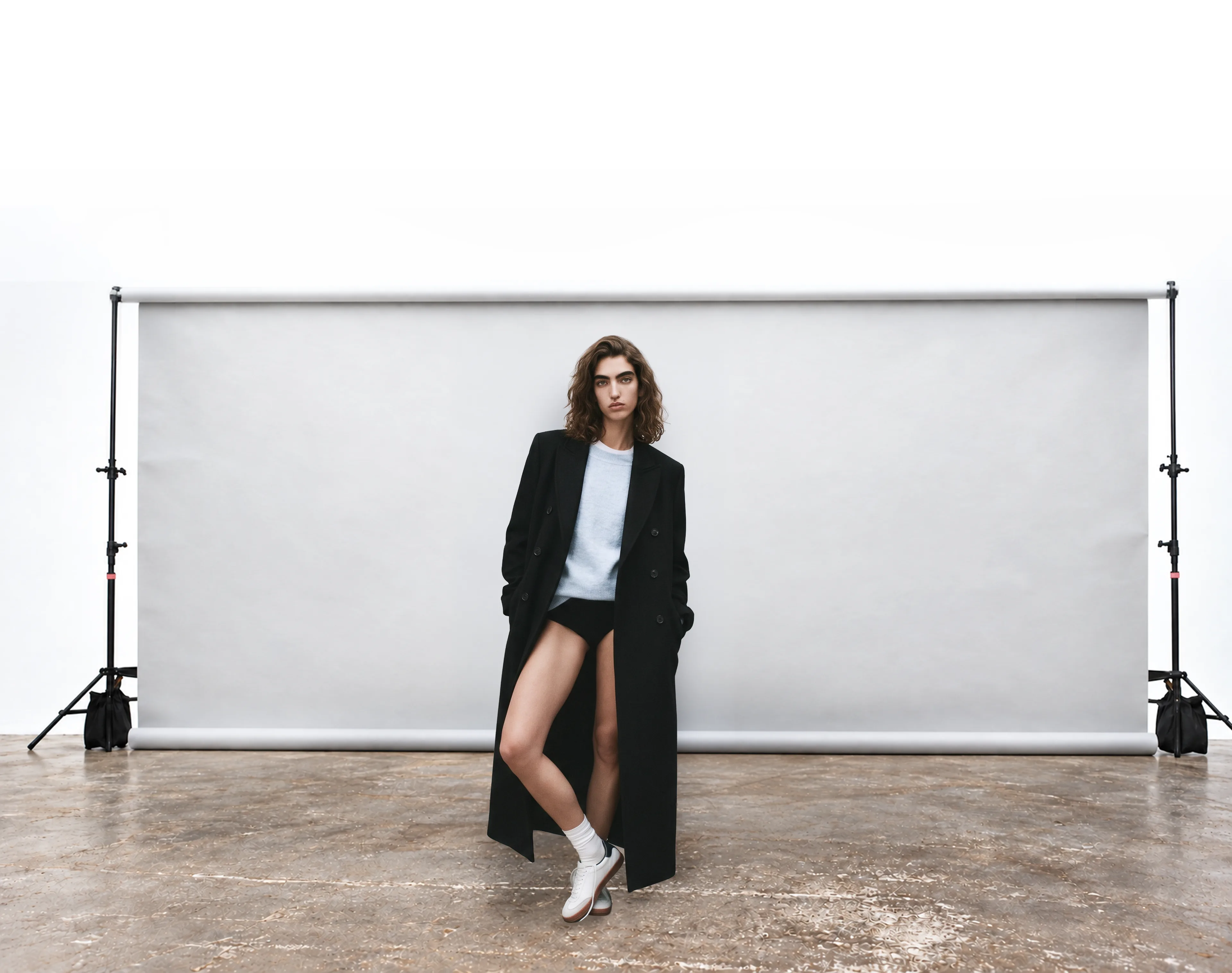 AI generated model in a long black coat standing in front of a grey backdrop in a photo studio