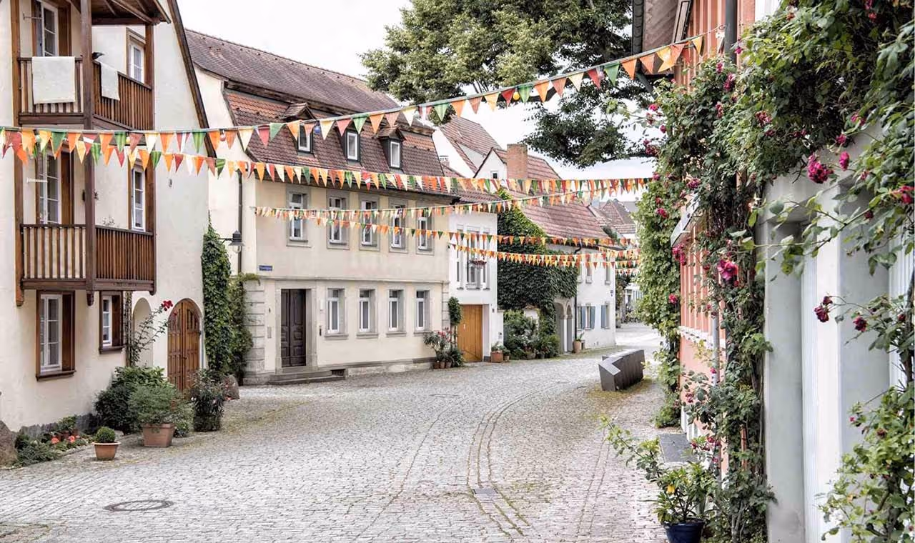 Cobblestone street with traditional European houses decorated with colorful triangular flags and flowering plants