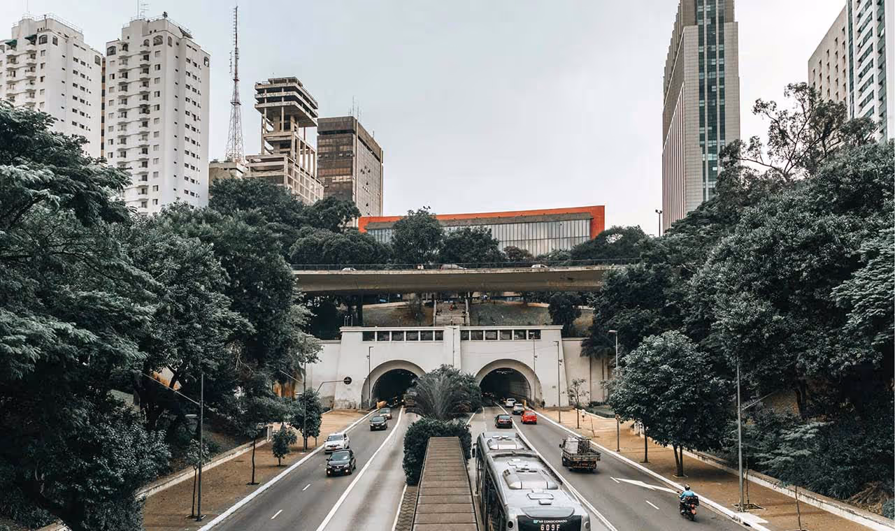 Vehicles driving through a dual tunnel underpass surrounded by trees and tall buildings