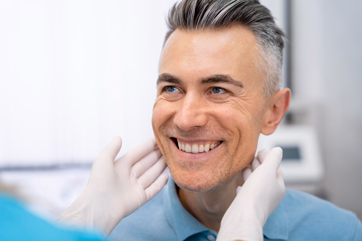 Doctor wearing gloves examining smiling middle-aged man's neck in a clinical setting.