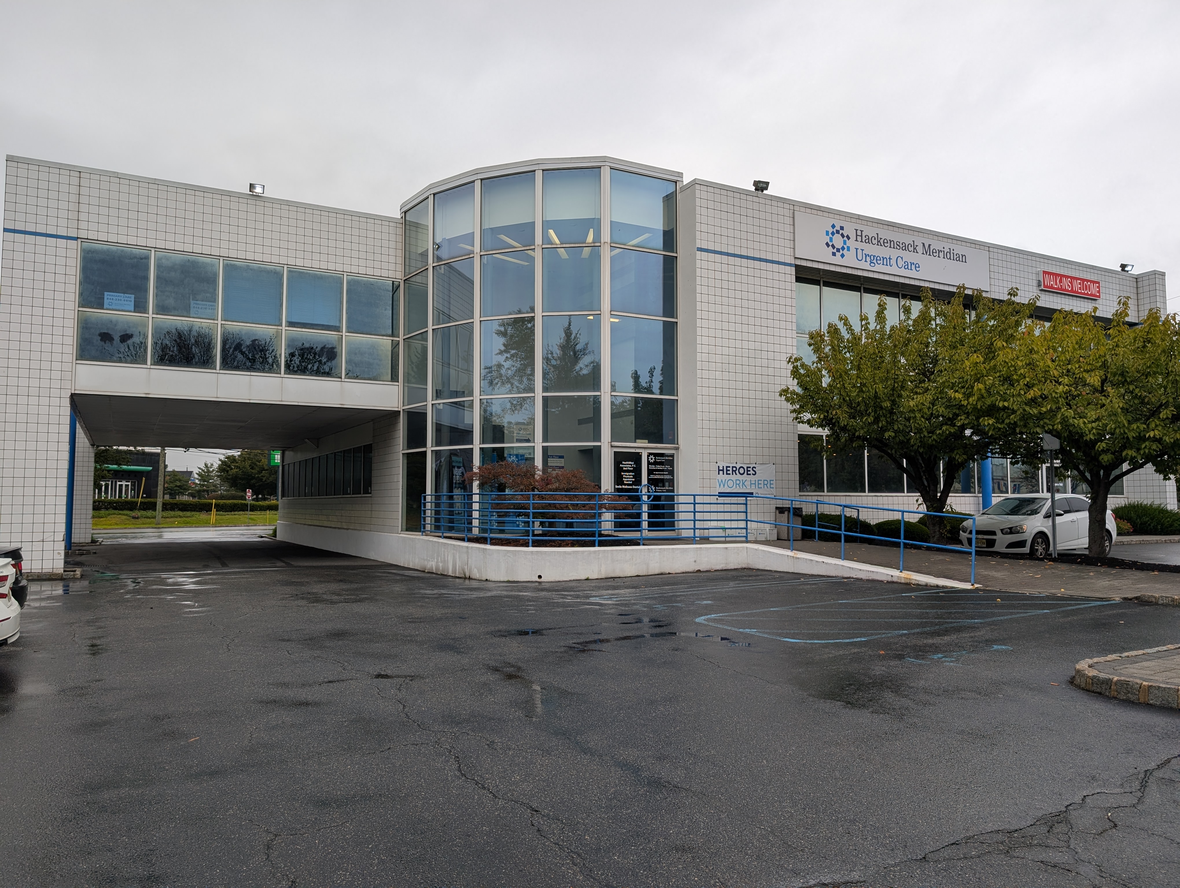 Hackensack Meridian Urgent Care building with ramp, parking, and trees on an overcast day.