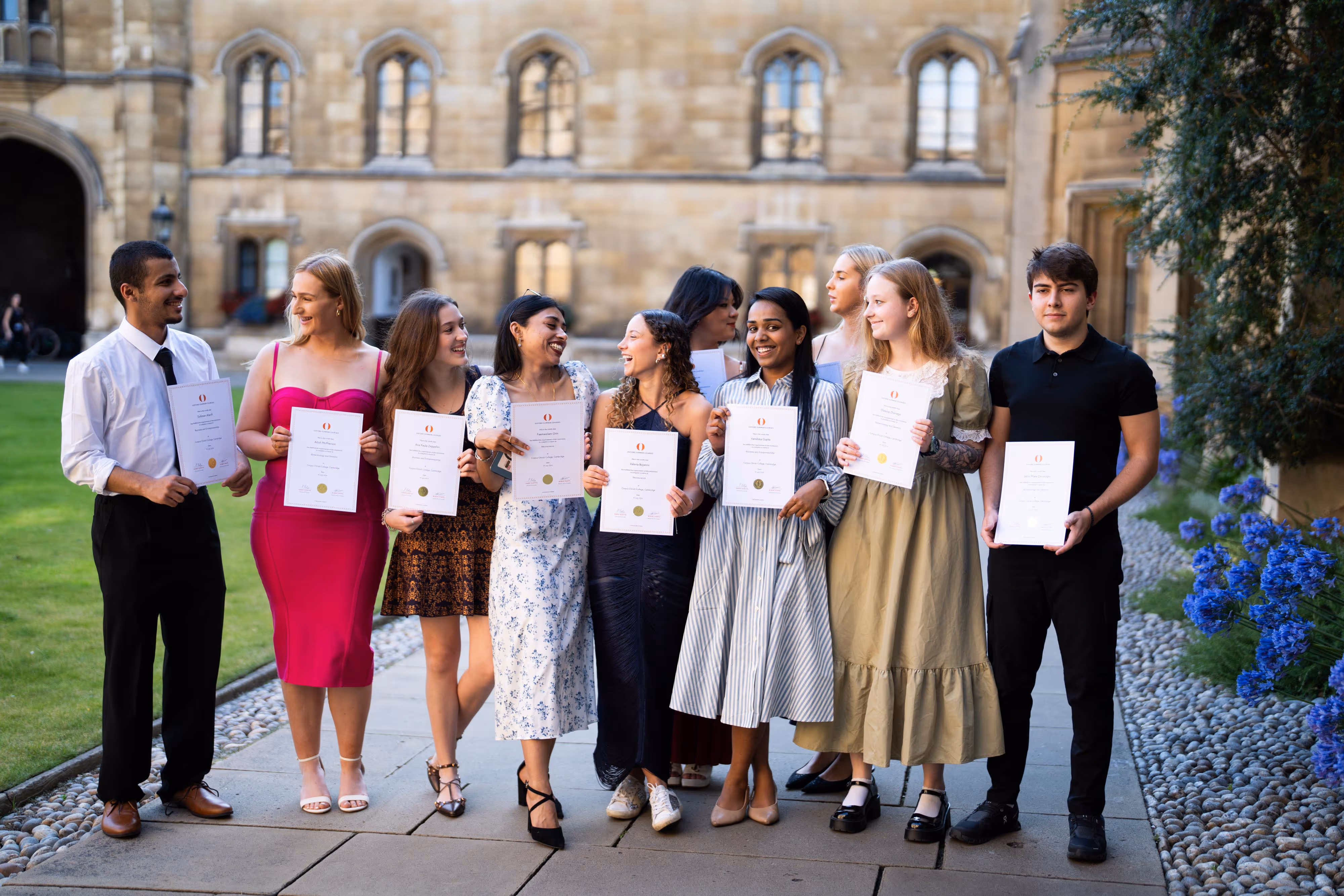 Group of young people holding certificates outdoors near a historic building