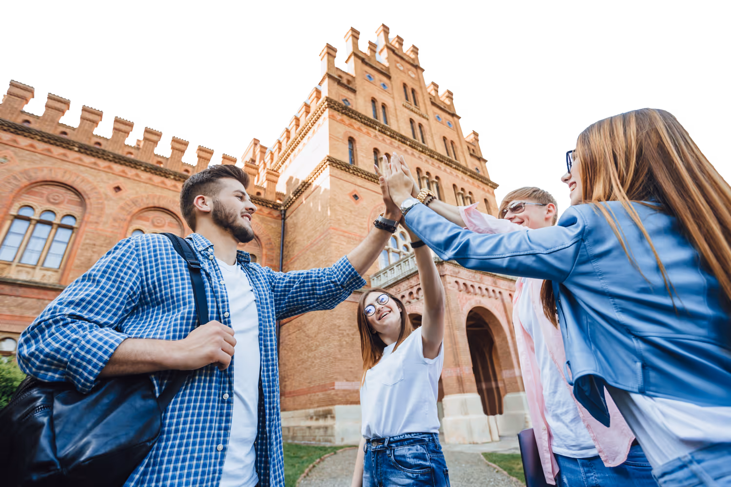 Group of four young adults giving a high-five outside a historic brick university building.