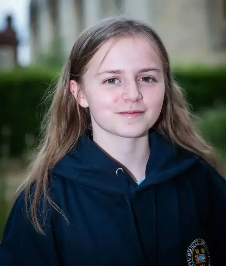 Young girl with long hair wearing a dark hoodie with a university emblem outdoors.