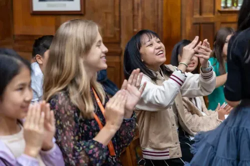 A group of diverse students clapping and smiling enthusiastically in a classroom setting.