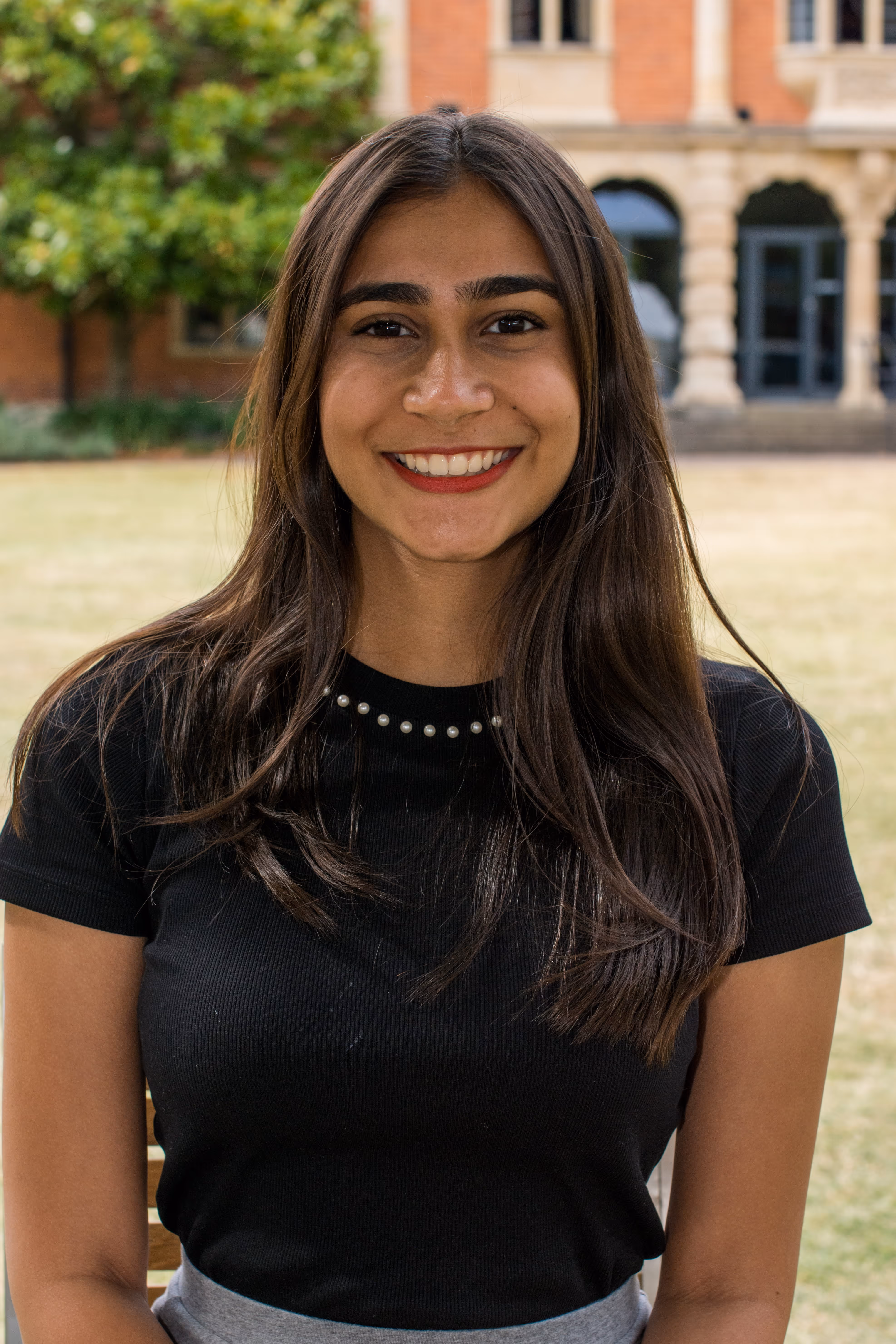Young man with glasses wearing a blue shirt smiling outdoors with a blurred background.