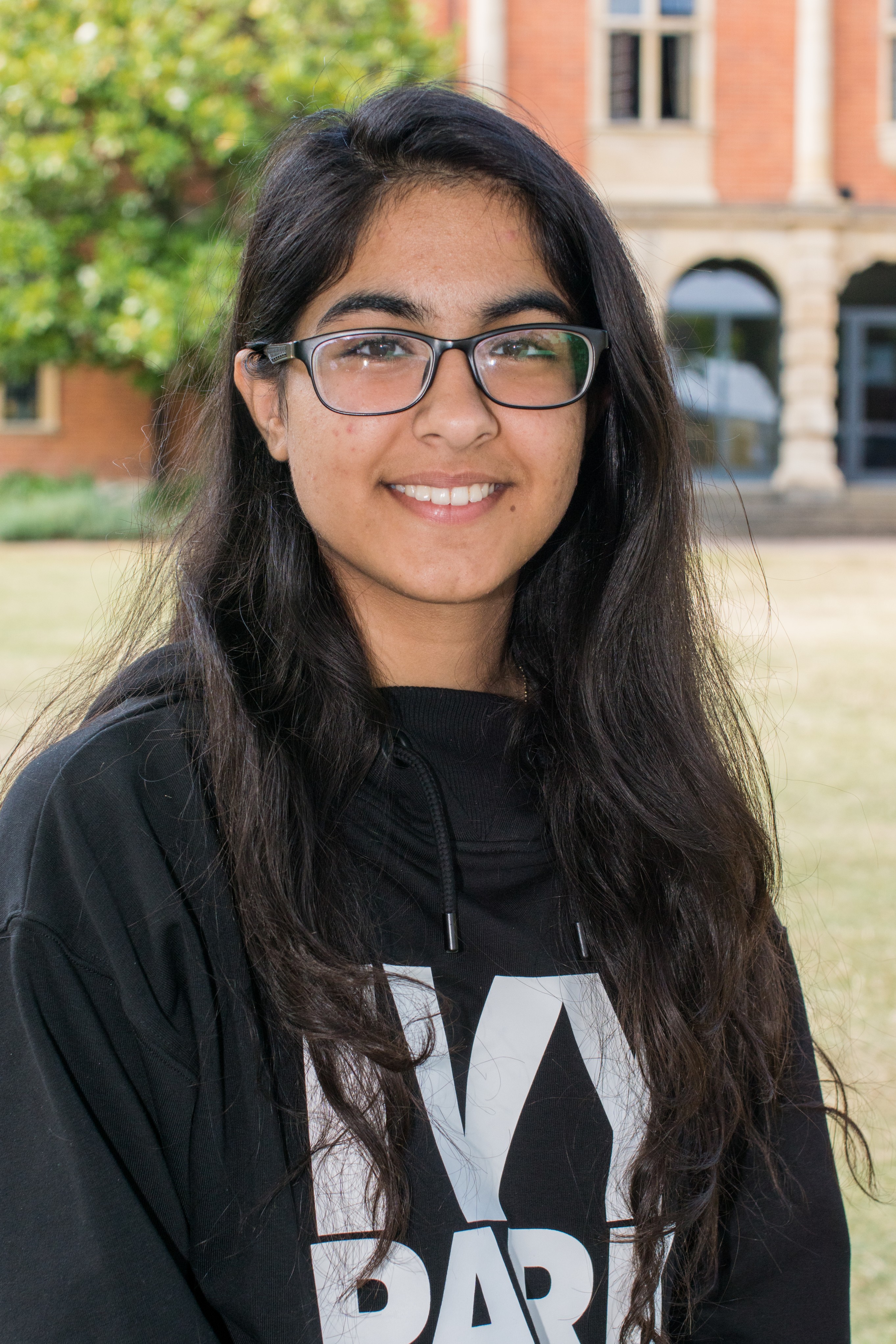 Young person with short brown hair and glasses smiling, wearing a blue shirt with white floral pattern.