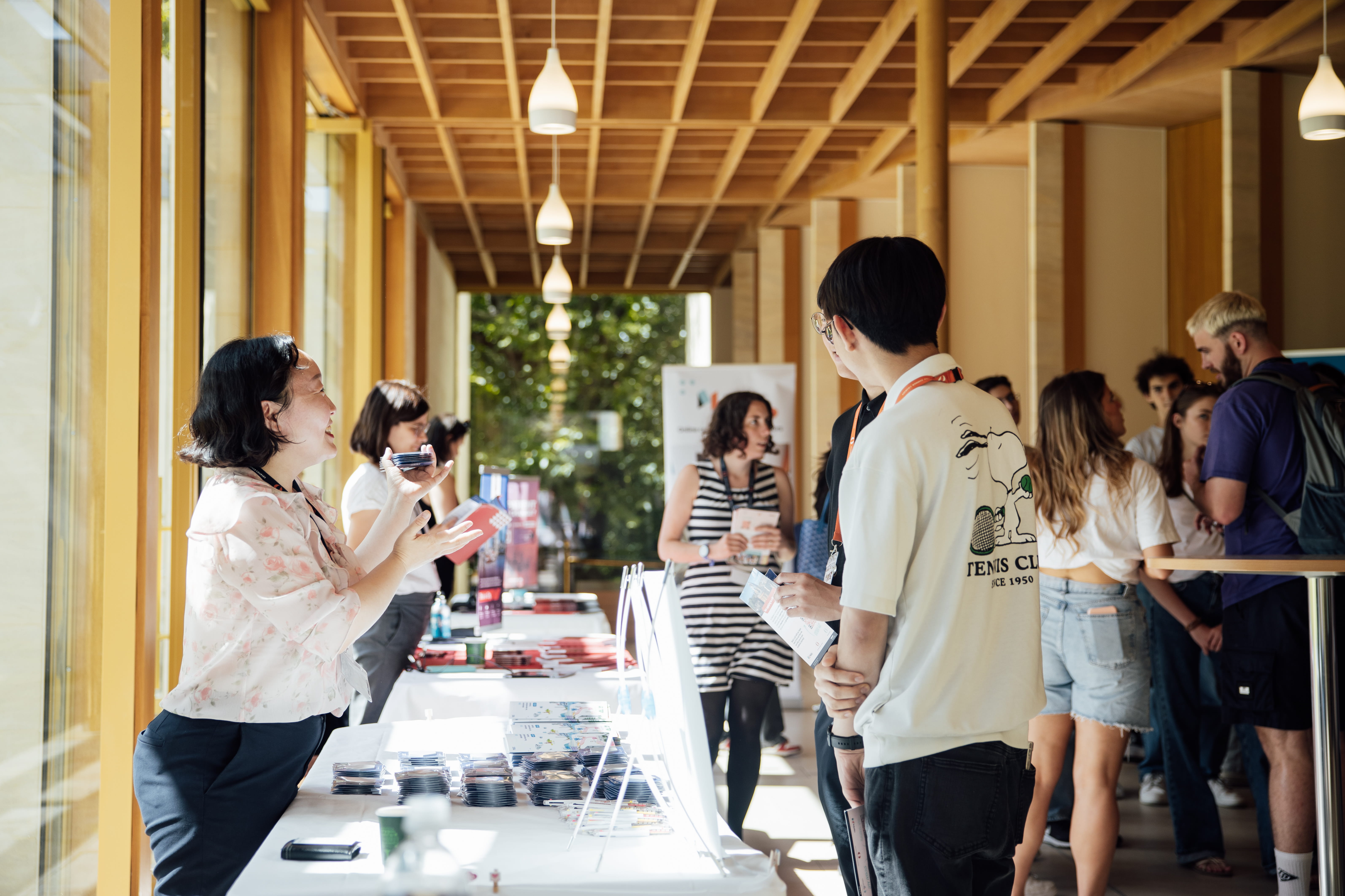 Two young people, a girl wearing glasses and a boy, attentively looking at a person gesturing outside the frame, outdoors with green foliage background.