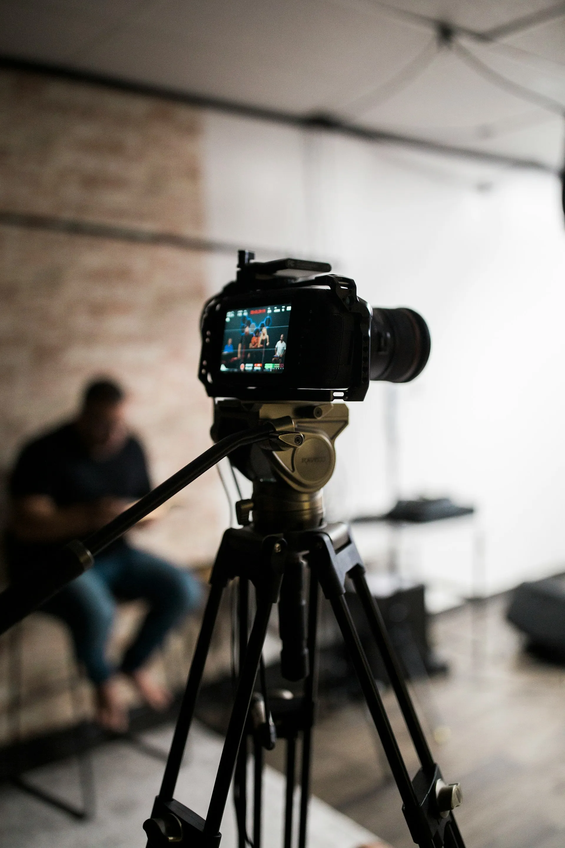 Camera on tripod recording a group of people sitting and talking in a room with blurred background.