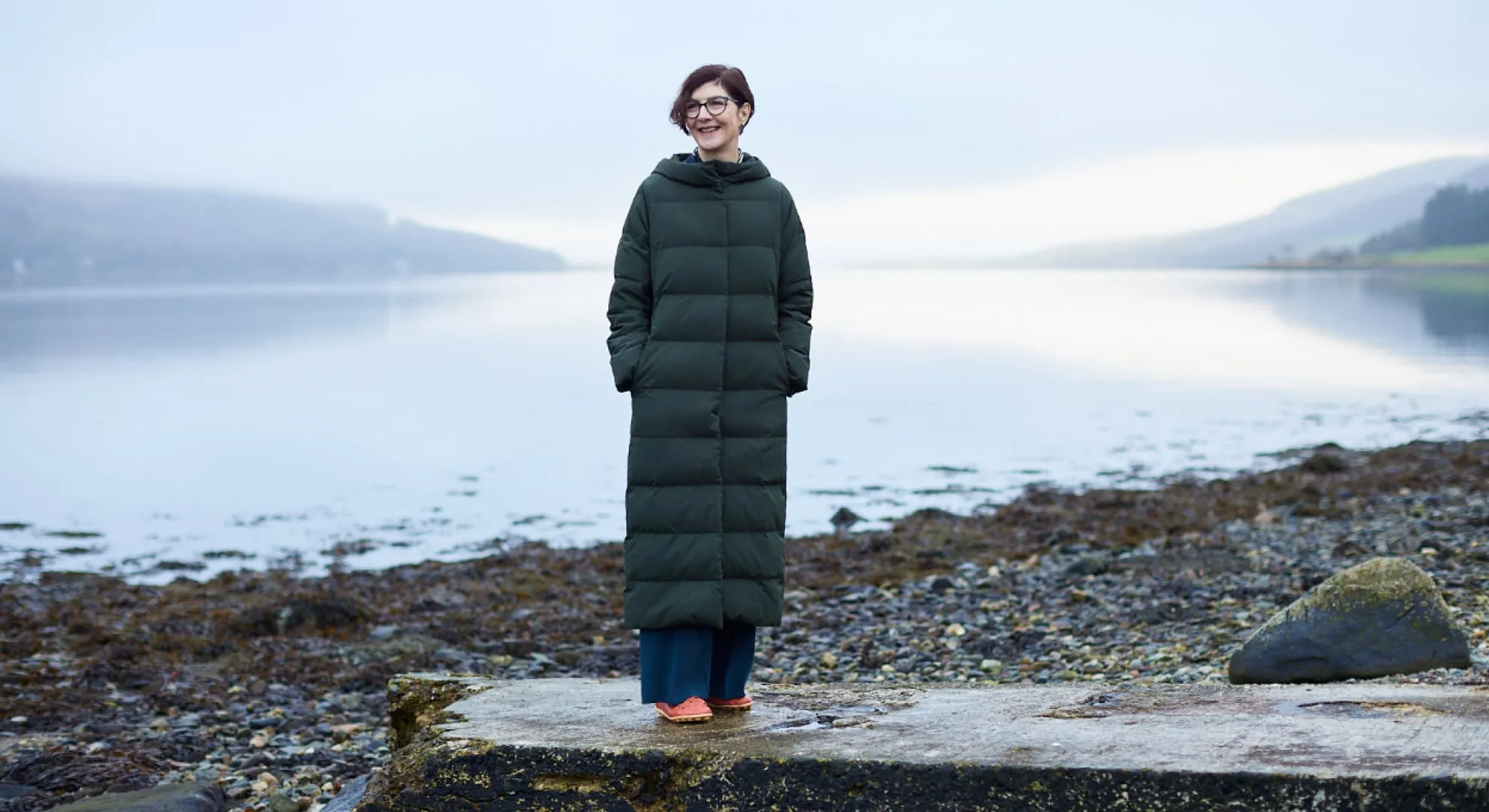 Lady standing smiling in front of the lake on a cold day