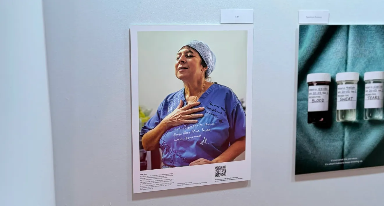 Exhibition wall at PM Society Awards 2026 showing a framed portrait of the woman in blue scrubs with a caption panel and QR code beneath the image.