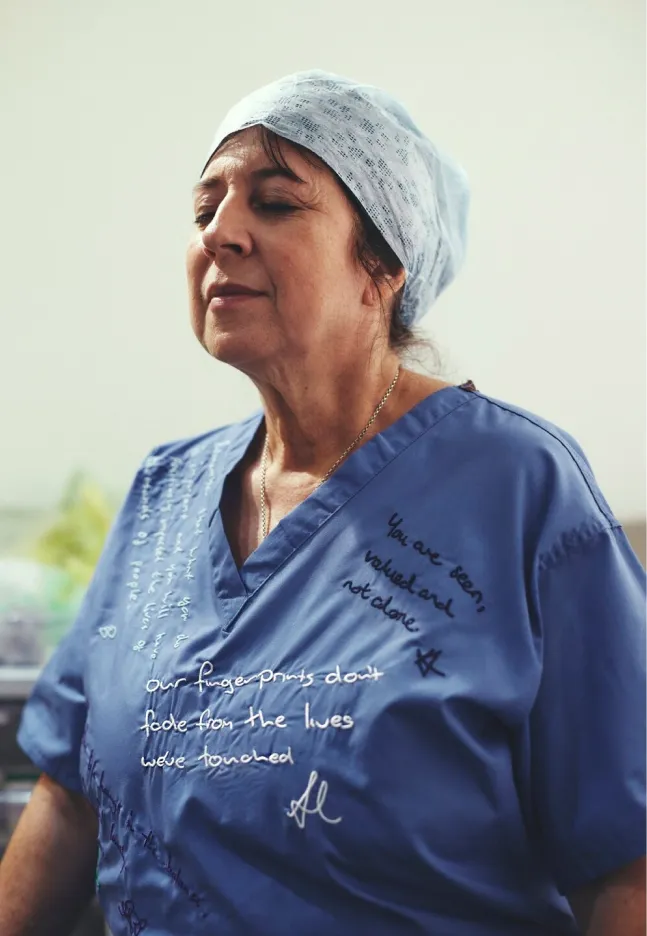 Portrait of a woman in blue scrubs and surgical cap, eyes closed, with messages visible across the front of her uniform.