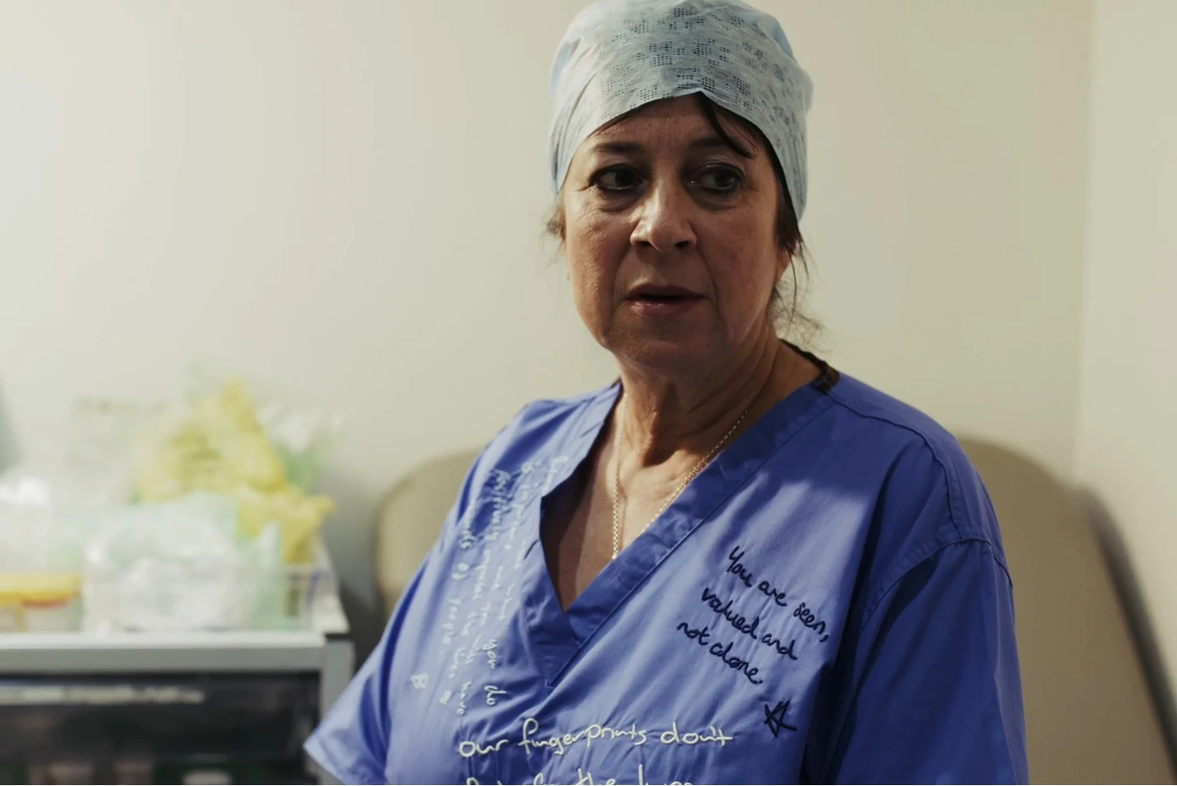 A woman in blue scrubs and surgical cap looking to one side, with supportive messages written across the fabric.