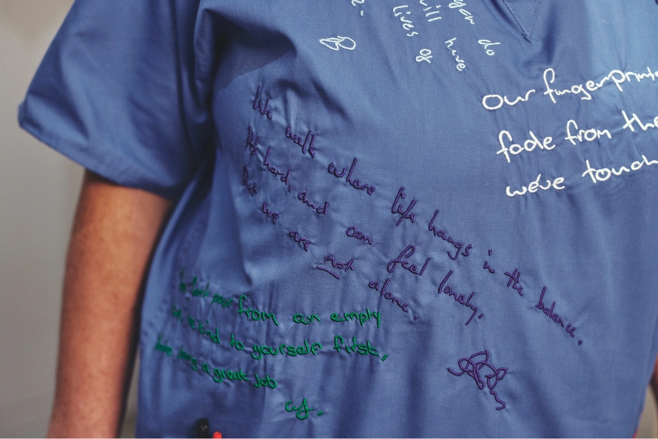 Angled close-up of blue scrubs showing multiple handwritten messages in purple and green across the front.