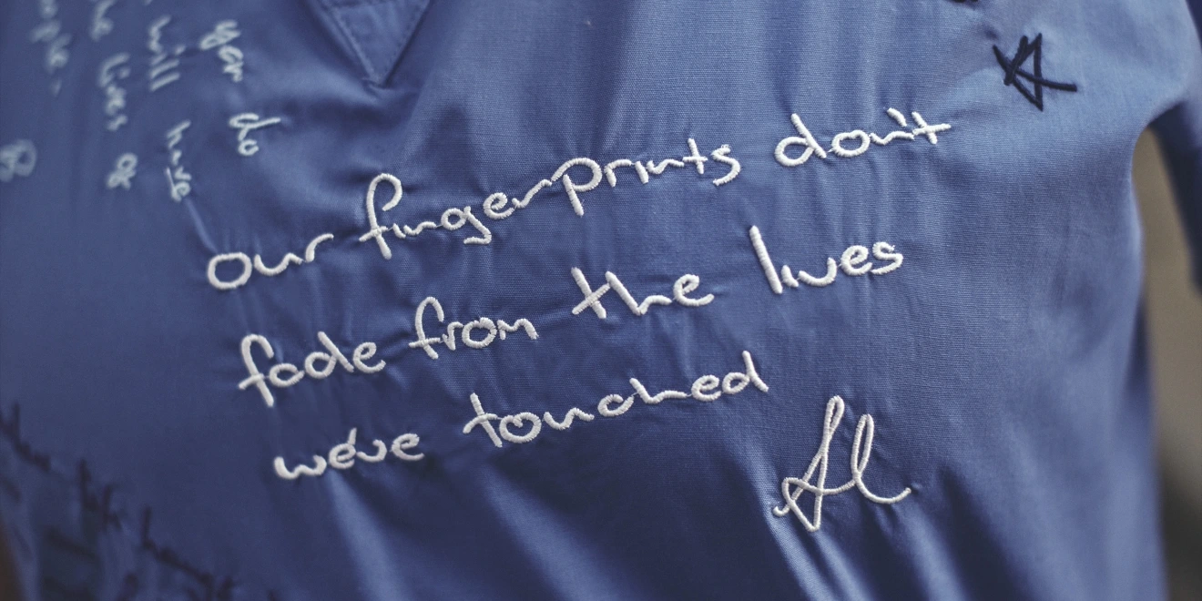 Close-up of blue scrubs embroidered with the words, “Our fingerprints don’t fade from the lives we’ve touched.”