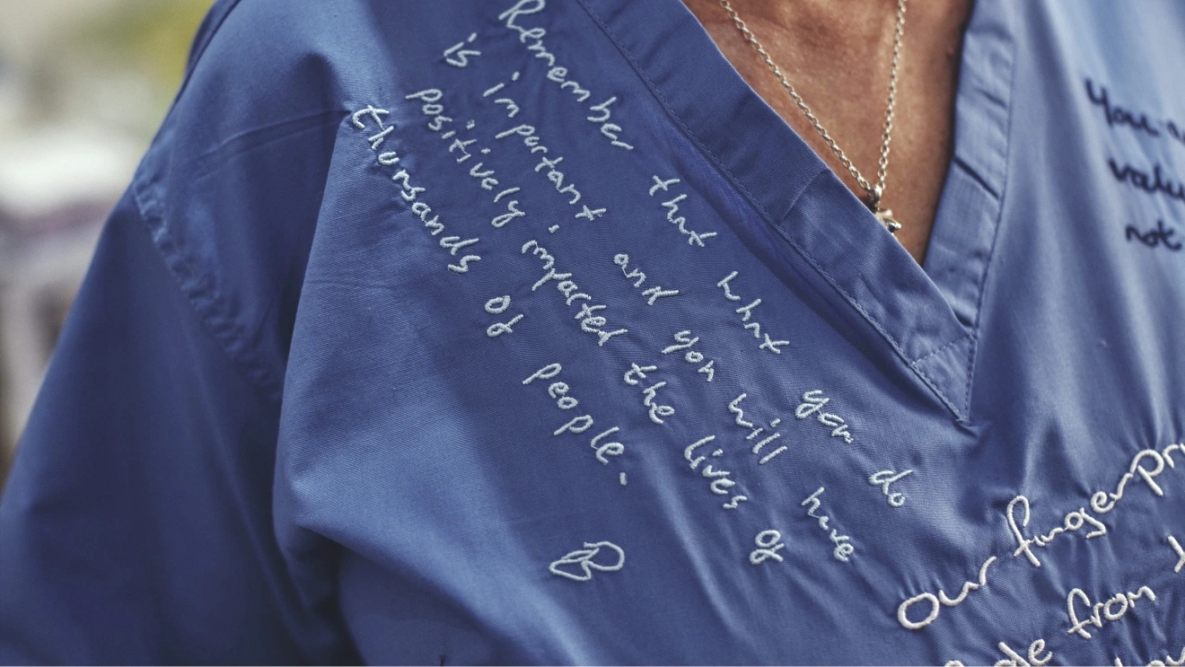 Close-up of the shoulder of blue scrubs with handwritten text about remaining positive and the lives of thousands of people.