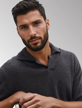 Headshot of Oliver, a male AI fashion model created by Botika, wearing a dark knit polo shirt sitting sideways on a chair. 