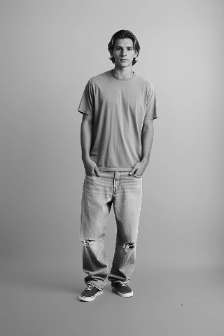A Botika male AI fashion model, Liam, in a black and white photo wearing an oversized tshirt and ripped jeans. 