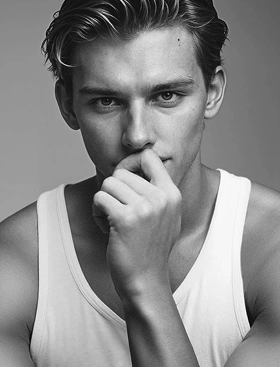 A black and white headshot of a Botika created male AI fashion model, Liam, wearing a white tank top with his hand at his mouth. 