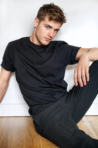A Botika male AI fashion model, Bran is sitting down lounging against a wall wearing an all black outfit. 