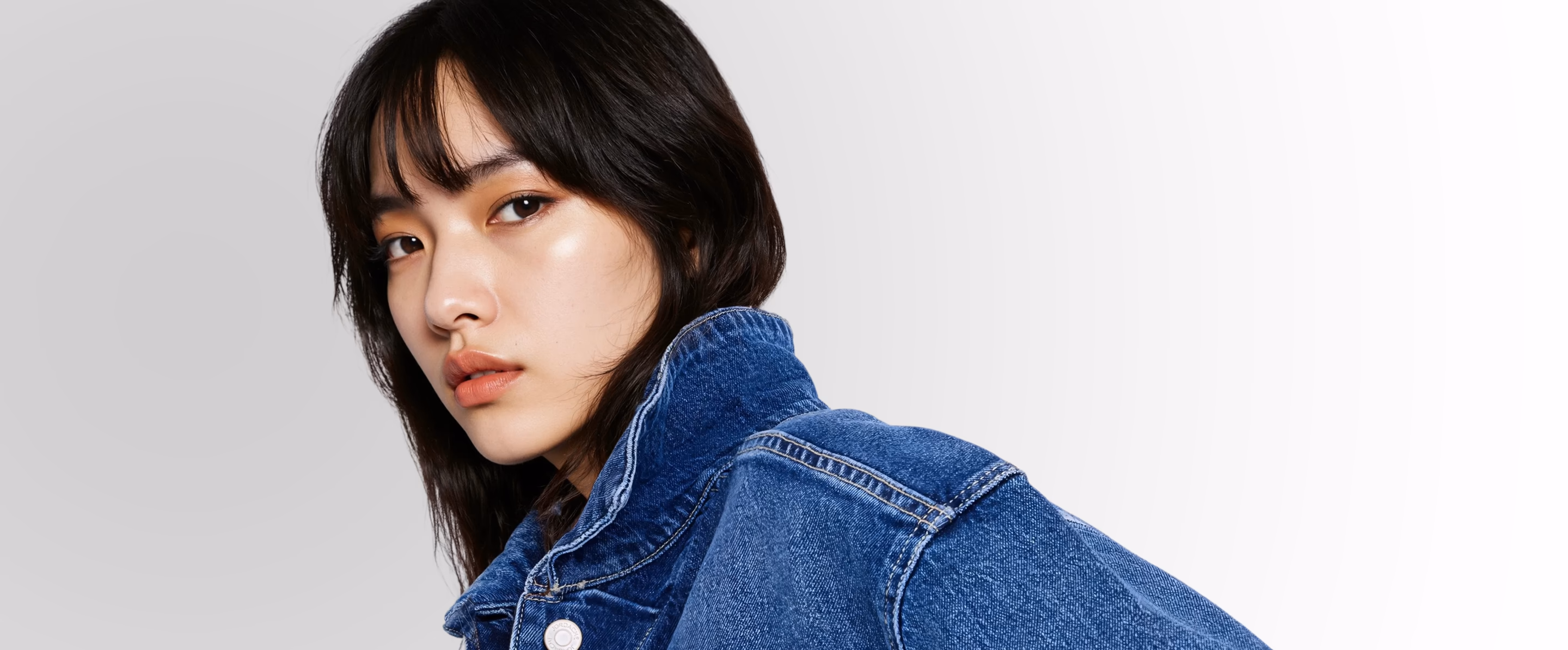 Blonde female AI generated fashion model wearing a jean jacket and a white tshirt.