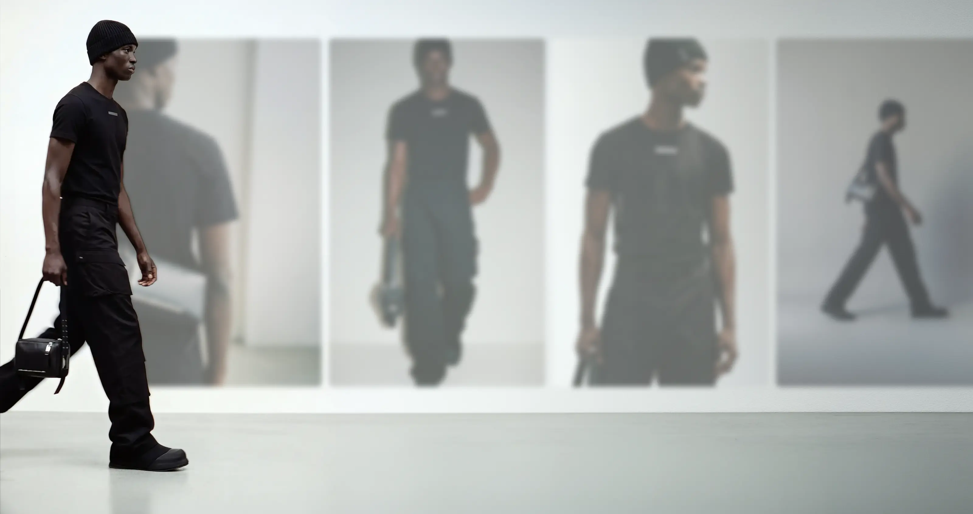 Image from HELIOT EMIL's Paris Fashion Week show containing their Botika custom AI fashion model walking a runway with product shots blurred behind him. 