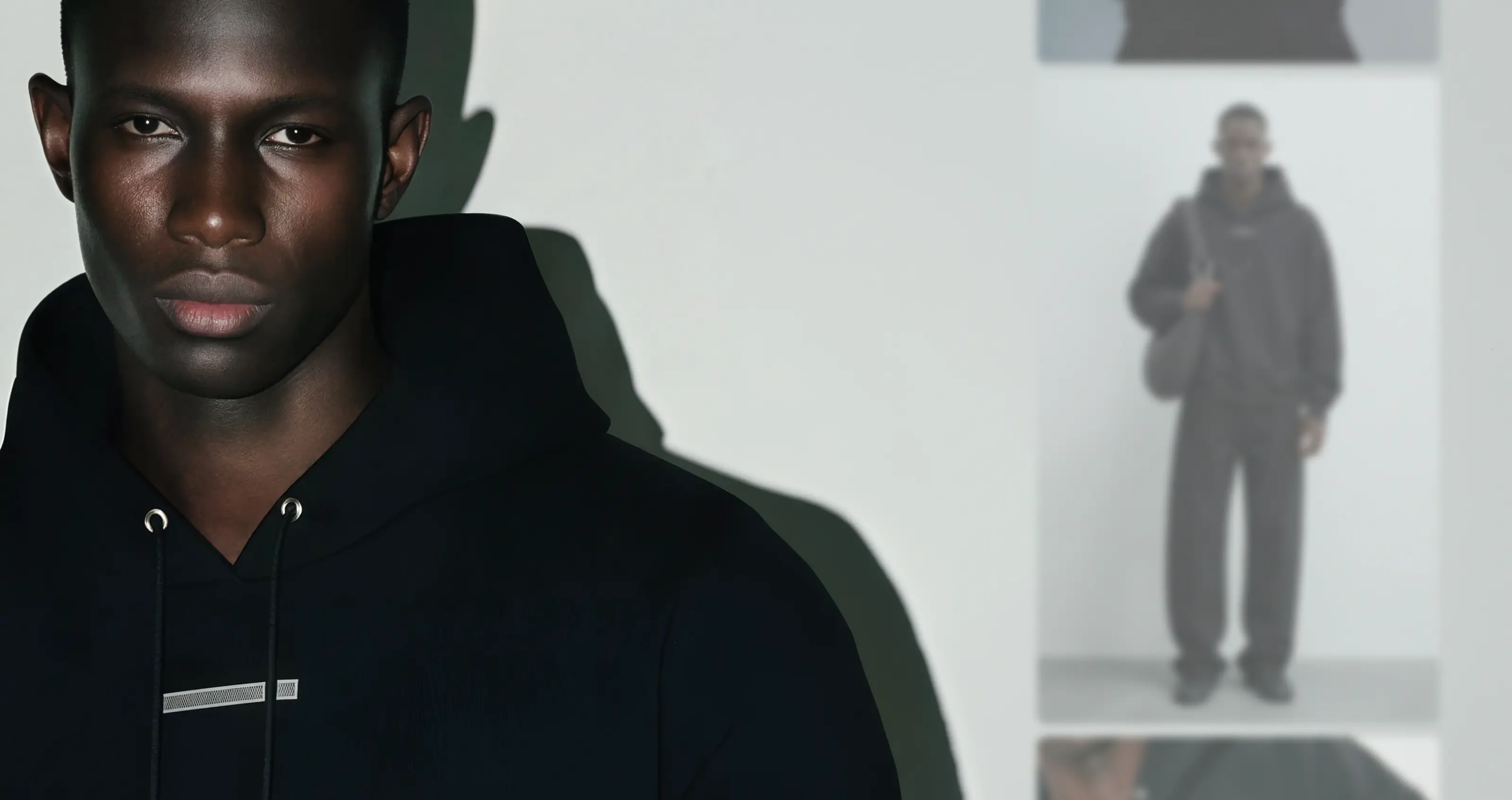 The HELIOT EMIL custom AI fashion model wearing a black sweatshirt on the left and on the right a blurred out filmstrip of the product images created for this outfit. 