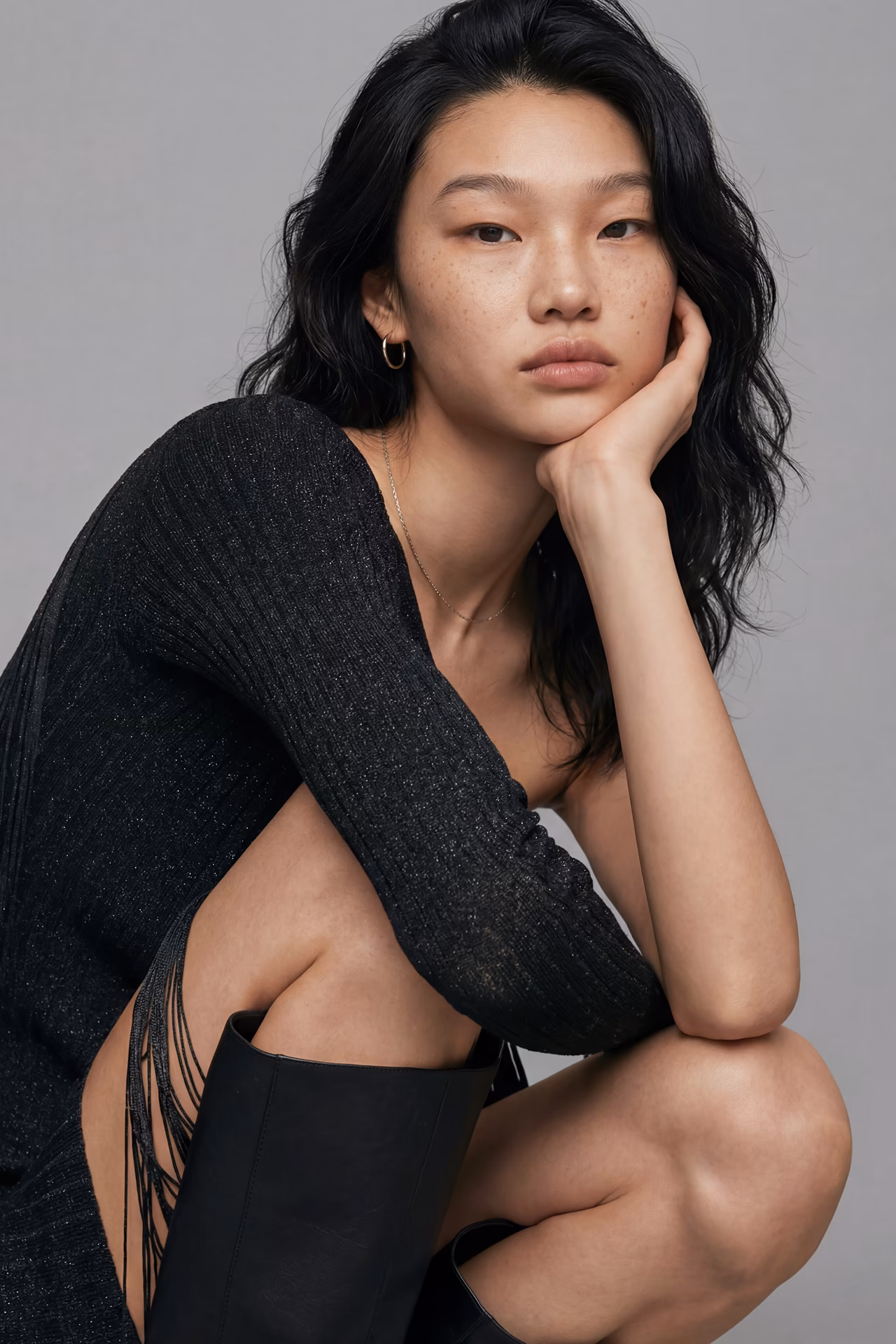 Yeo Jin, an Asian female AI fashion model crouching wearing an off the shoulder black top and boots.