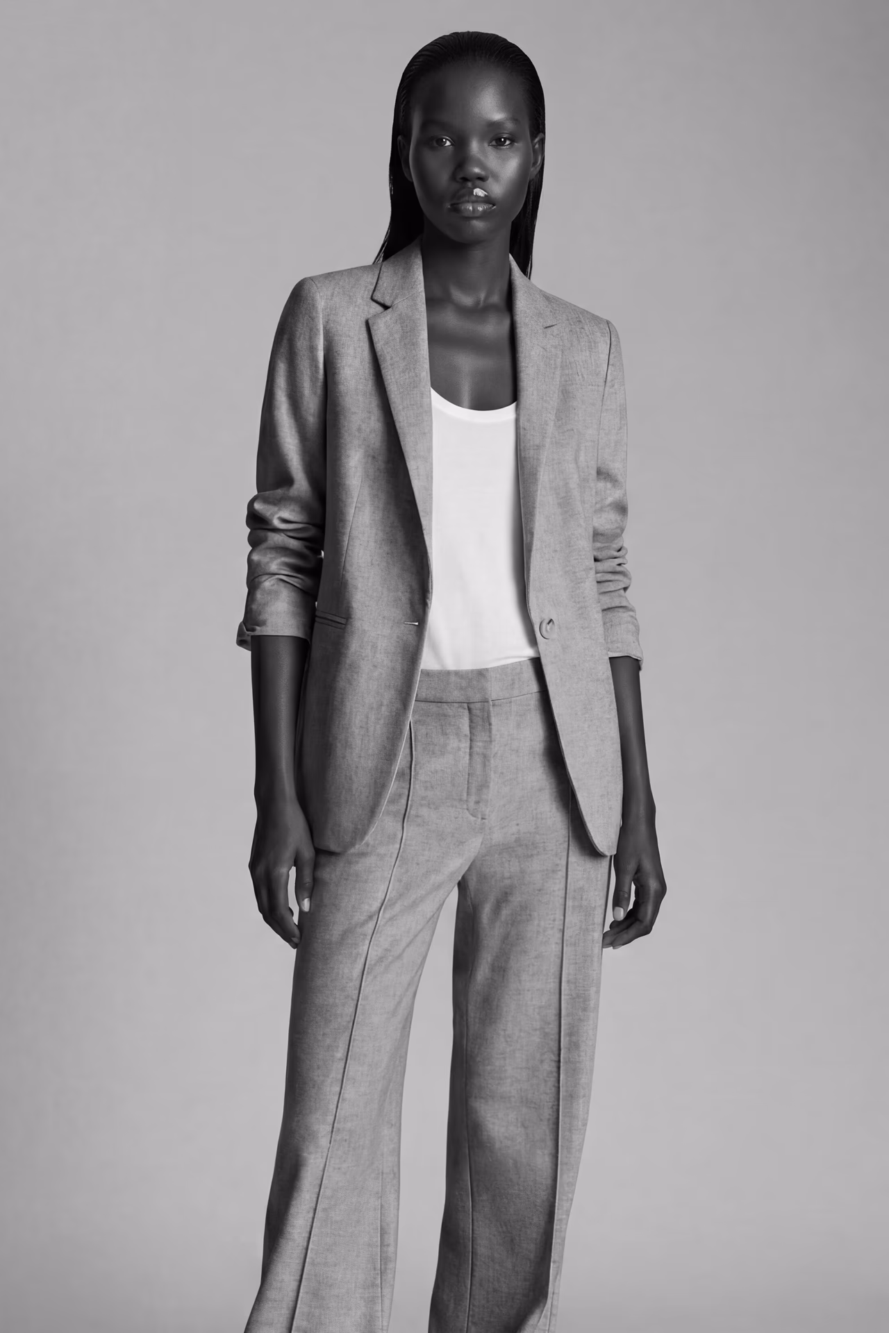A black female AI fashion model named Ayo wearing a light suite with white tank top standing in a black and white product photo.