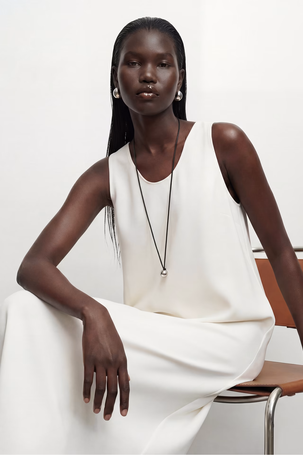 Ayo, a black female AI fashion model created by Botika wearing a white flowing dress while sitting.