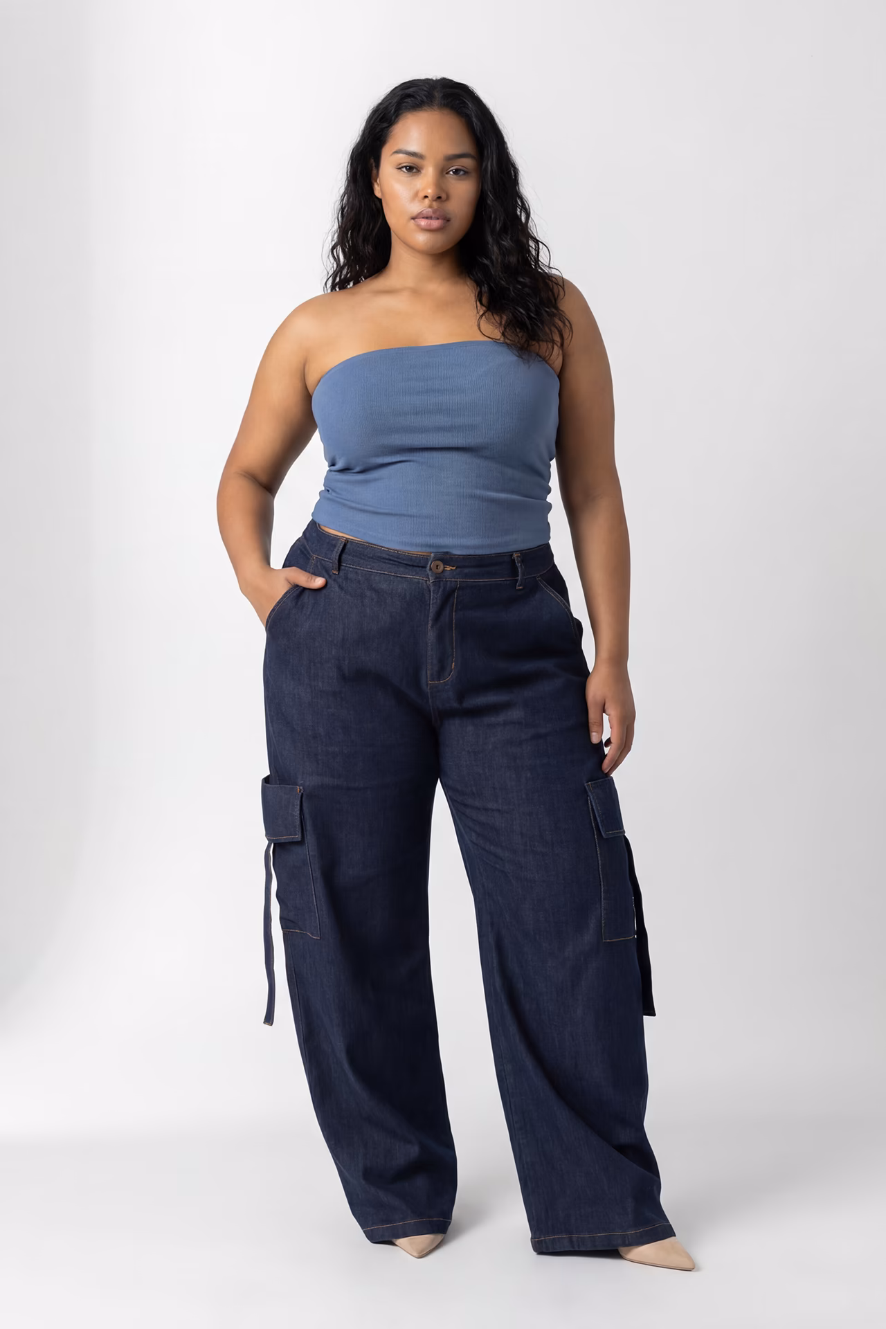 Leni, a plus sized Latina AI generated model is standing wearing a light blue crop top and dark blue cargo style pants.