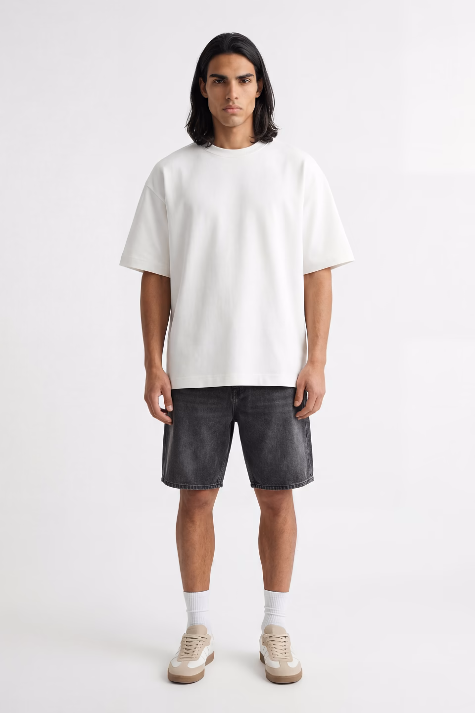 Giovanni, Botika's long dark haired male AI fashion model wearing an oversized white tshirt, washed black denim shorts and sneakers.