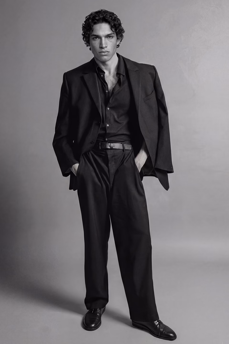 A black and white full body model shot of Rodrigo, a Botika make AI fashion model wearing a dark suit with a dark suit.